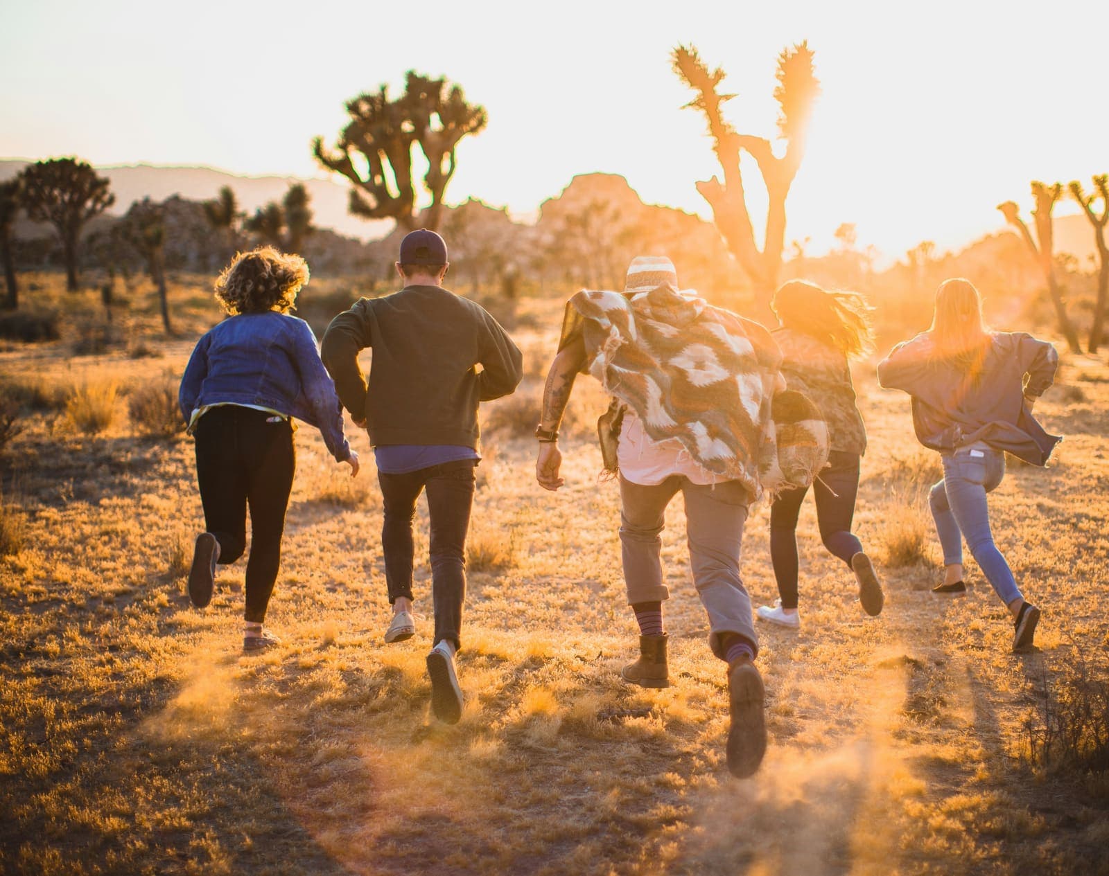 Five friends running together through a field at sunset